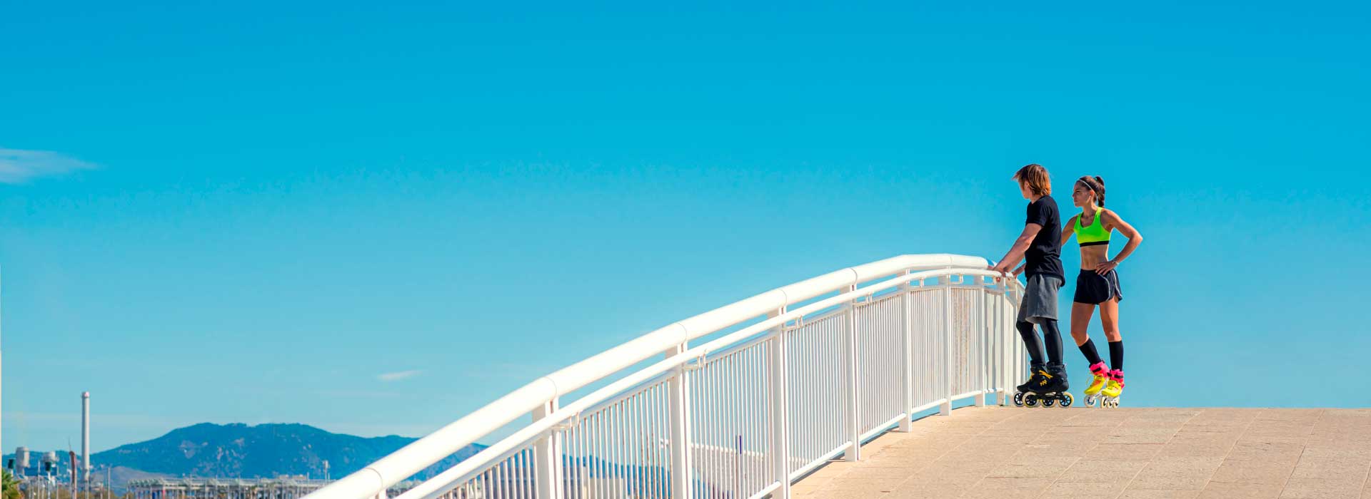 A male and female are standing on a bridge looking at the horizon while wearing Powerslide inline skates